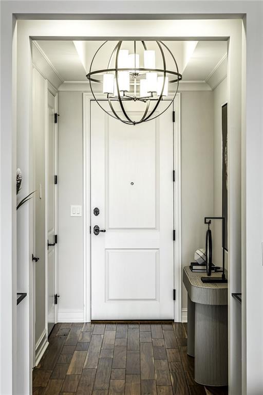 doorway to outside featuring baseboards, dark wood-style flooring, a chandelier, and ornamental molding