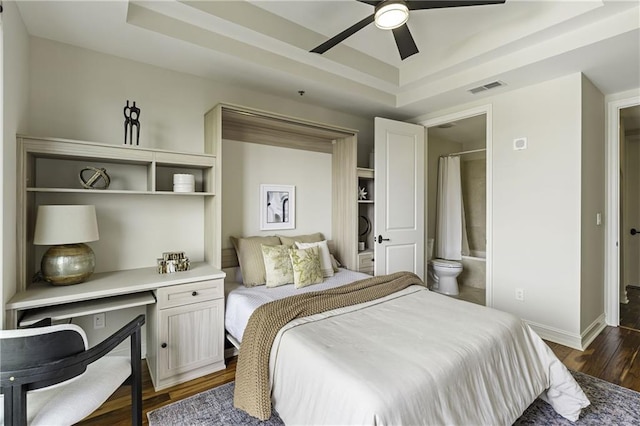 bedroom with a tray ceiling, baseboards, visible vents, and dark wood-style flooring