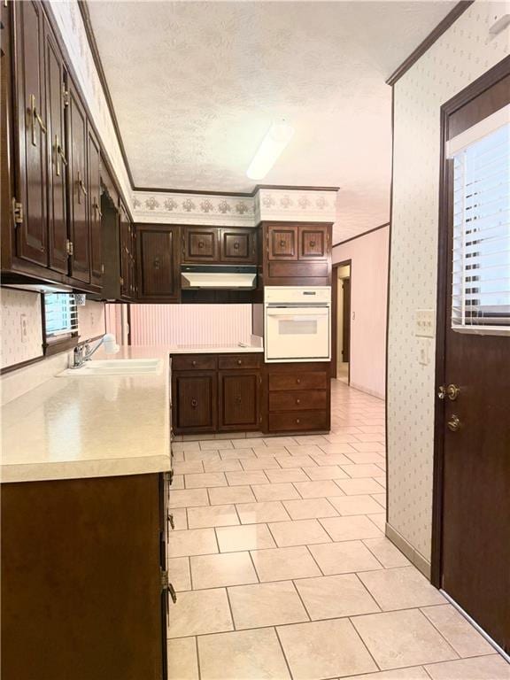 10 Montre Cir, Silver Creek, GA 30173 - kitchen featuring oven, wallpapered walls, under cabinet range hood, crown molding, and light countertops