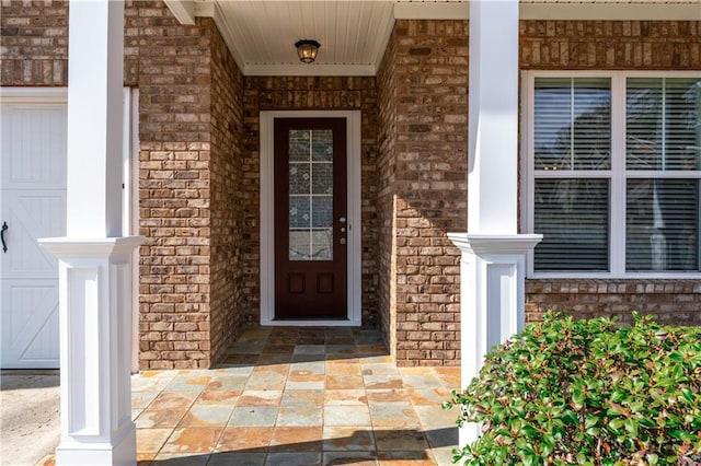 view of exterior entry with a garage and brick siding