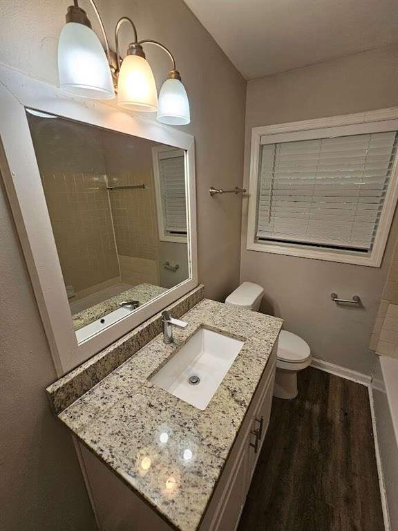 bathroom featuring tiled shower, vanity, toilet, and hardwood / wood-style flooring