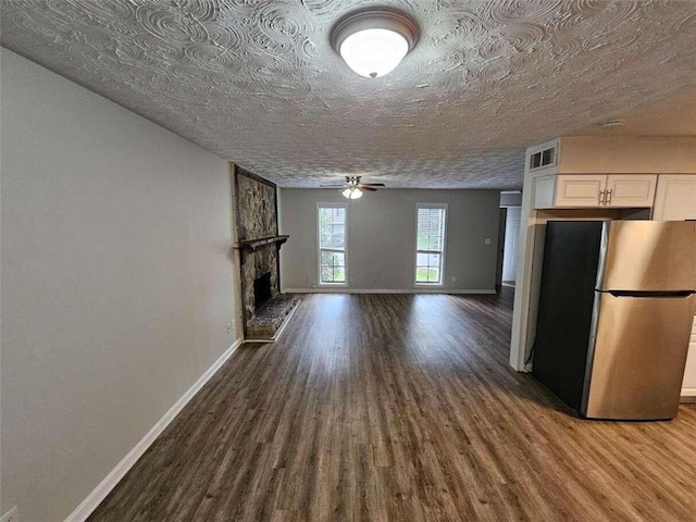 kitchen featuring stainless steel fridge, a textured ceiling, white cabinetry, a large fireplace, and hardwood / wood-style floors