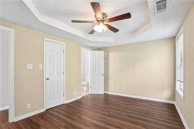 1039 Megan Ct, Sugar Hill, GA 30518 - unfurnished bedroom featuring a tray ceiling, a textured ceiling, dark wood finished floors, baseboards, and ensuite bath