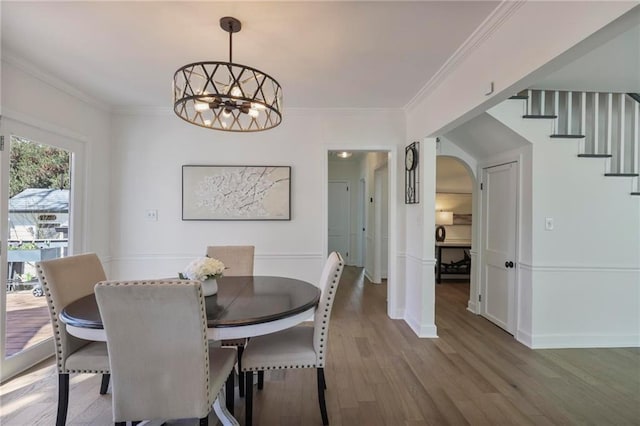 dining area featuring an inviting chandelier, crown molding, wood finished floors, and arched walkways