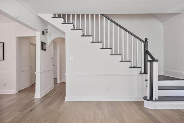 stairs featuring arched walkways, crown molding, and wood finished floors