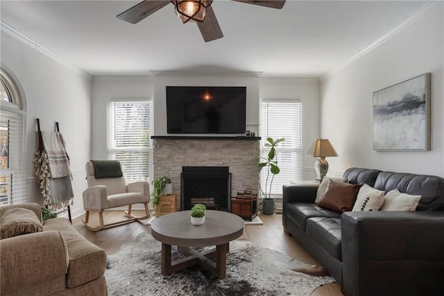 living room with a ceiling fan, wood finished floors, crown molding, and a fireplace