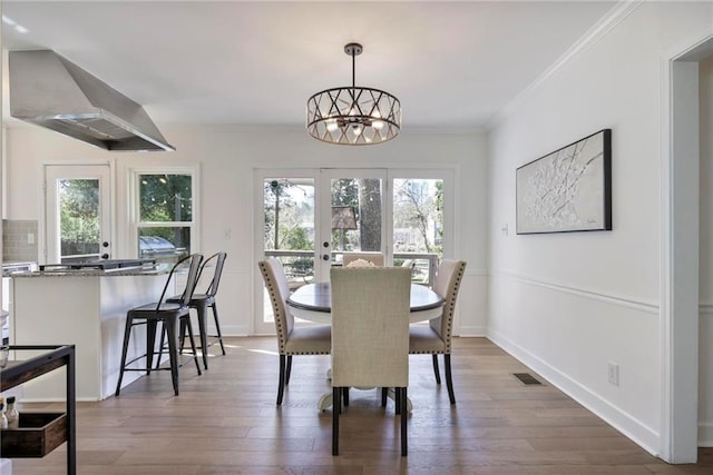 dining area with french doors, crown molding, an inviting chandelier, and wood finished floors