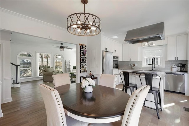 dining room with light wood-type flooring, a healthy amount of sunlight, ornamental molding, and stairs