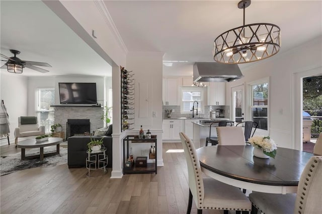 dining room with light wood-style flooring, ceiling fan with notable chandelier, a fireplace, crown molding, and baseboards