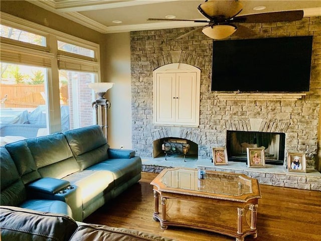 living room with hardwood / wood-style flooring, ceiling fan, a stone fireplace, and crown molding