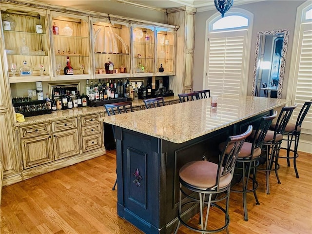 bar featuring light wood-type flooring, light stone counters, hanging light fixtures, and ornamental molding