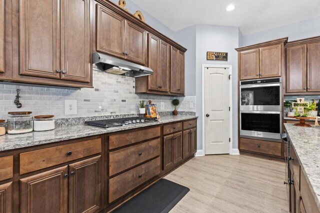 kitchen featuring stainless steel appliances, light stone counters, light hardwood / wood-style floors, and tasteful backsplash