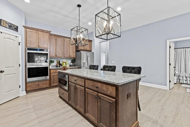 kitchen with a breakfast bar, a kitchen island, pendant lighting, stainless steel appliances, and light wood-type flooring