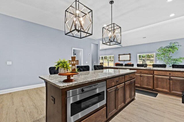 kitchen with dark brown cabinets, pendant lighting, light stone counters, a center island, and light hardwood / wood-style flooring