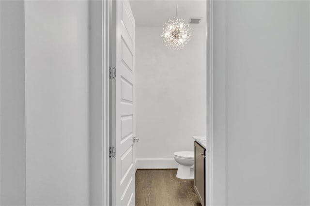 bathroom featuring wood-type flooring, toilet, vanity, and a notable chandelier