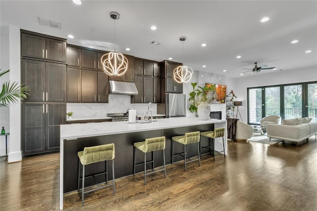 kitchen featuring a breakfast bar, stainless steel fridge, hanging light fixtures, a large island, and dark brown cabinetry