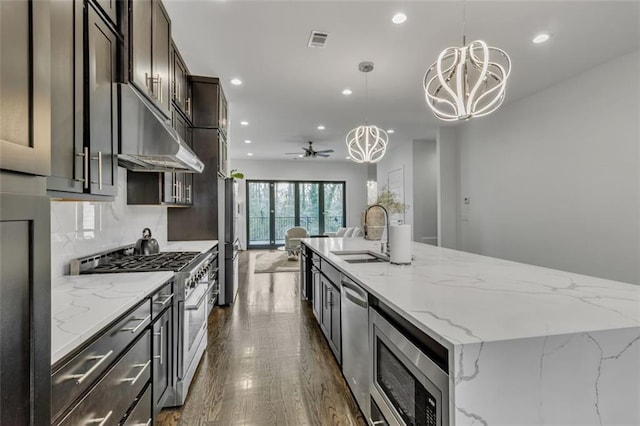 kitchen featuring appliances with stainless steel finishes, decorative light fixtures, sink, light stone counters, and a spacious island