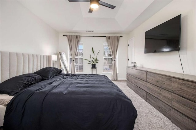 carpeted bedroom with ceiling fan and a tray ceiling