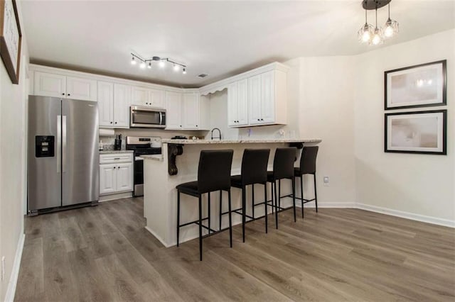 kitchen featuring a breakfast bar, kitchen peninsula, pendant lighting, stainless steel appliances, and white cabinets