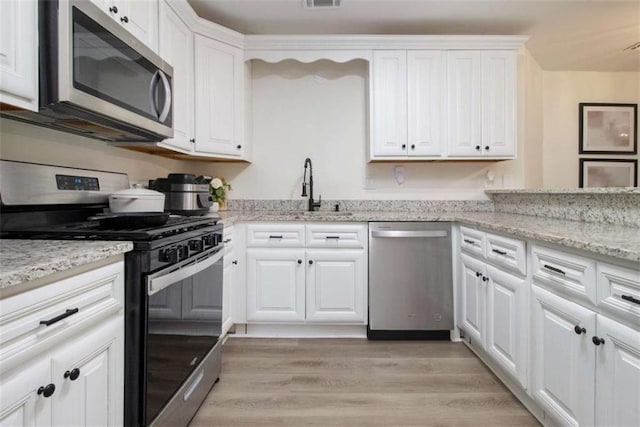 kitchen featuring sink, light stone counters, light hardwood / wood-style flooring, stainless steel appliances, and white cabinets