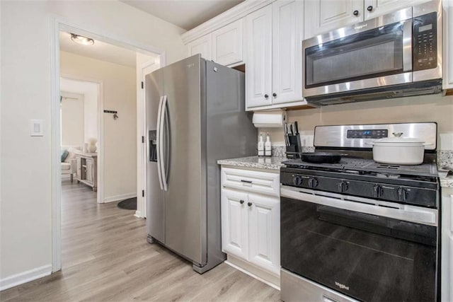 kitchen featuring light stone countertops, white cabinetry, appliances with stainless steel finishes, and light wood-type flooring