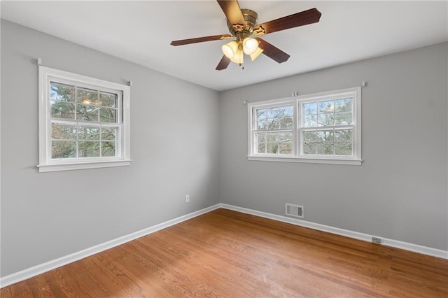 unfurnished room featuring visible vents, plenty of natural light, baseboards, and wood finished floors