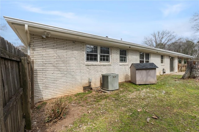 back of property featuring a storage shed, brick siding, fence, and central air condition unit