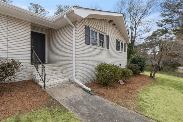 property entrance with brick siding and a lawn