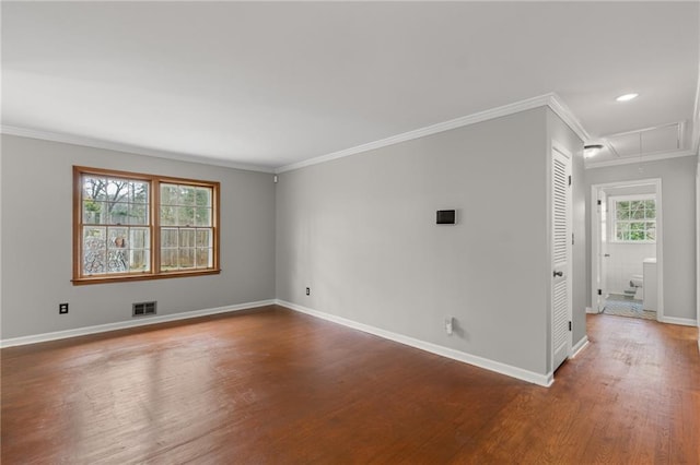 unfurnished room with wood finished floors, visible vents, baseboards, attic access, and crown molding