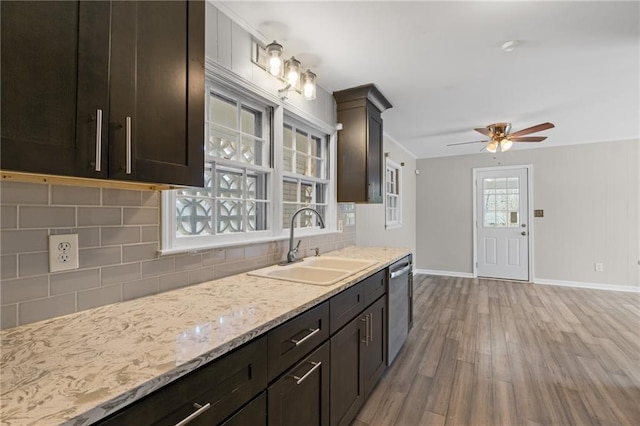 kitchen featuring light wood-style flooring, decorative backsplash, stainless steel dishwasher, a sink, and baseboards