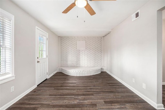 empty room featuring ceiling fan, dark wood-type flooring, and brick wall