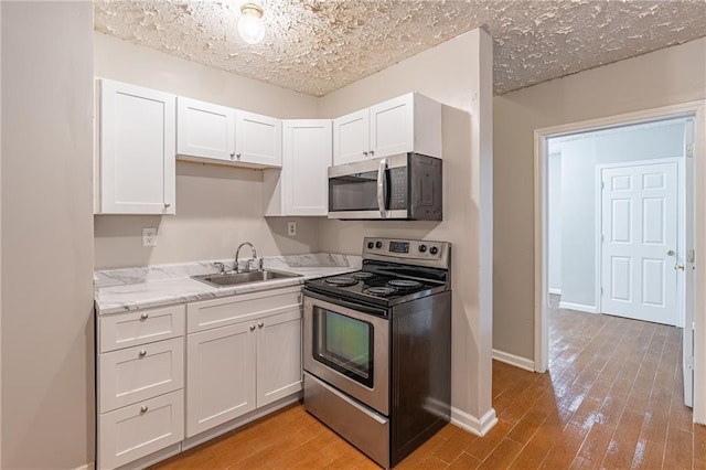 1241 Hogan Ridge Ct, Grayson, GA 30017 - kitchen with appliances with stainless steel finishes, a sink, white cabinetry, light wood-style flooring, and baseboards