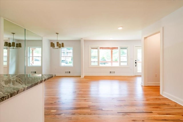 unfurnished living room featuring an inviting chandelier and light hardwood / wood-style floors