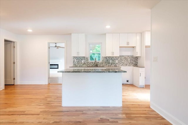 kitchen featuring white cabinetry, tasteful backsplash, dark stone countertops, and light wood-type flooring