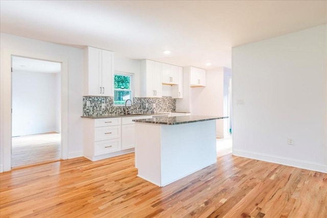 kitchen with tasteful backsplash, sink, white cabinets, and light wood-type flooring