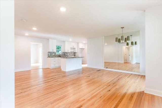 unfurnished living room with an inviting chandelier, sink, and light hardwood / wood-style flooring