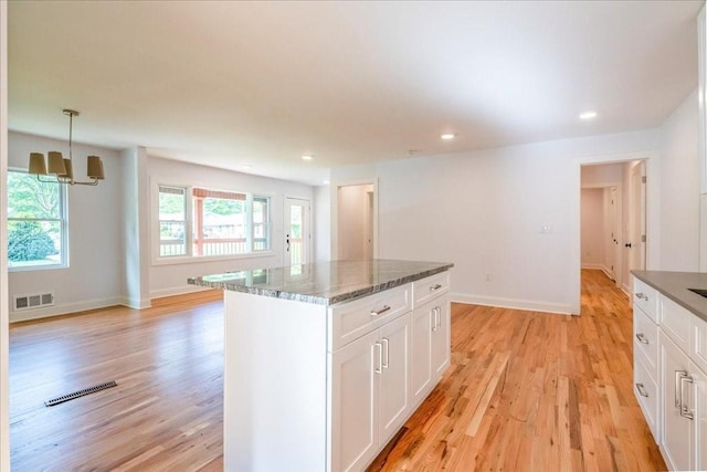 kitchen with a kitchen island, white cabinetry, dark stone counters, hanging light fixtures, and light hardwood / wood-style floors