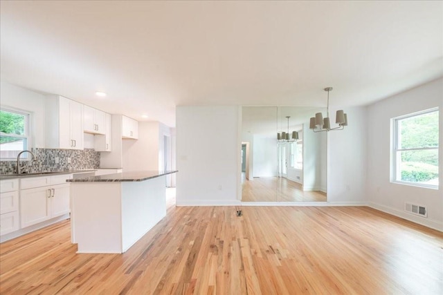 kitchen featuring white cabinetry, sink, decorative backsplash, hanging light fixtures, and light hardwood / wood-style floors