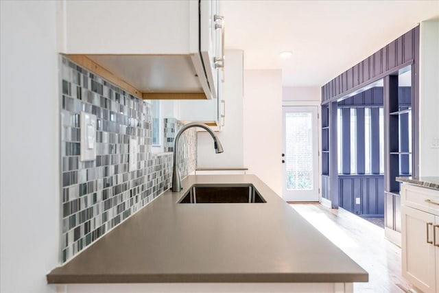 kitchen featuring tasteful backsplash, white cabinetry, sink, light hardwood / wood-style floors, and kitchen peninsula