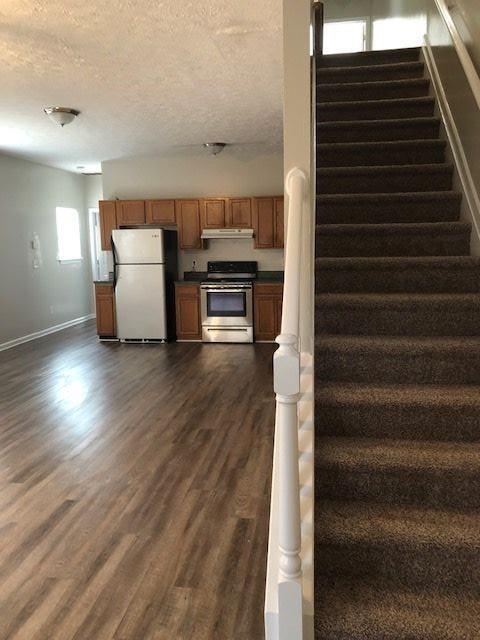 kitchen with a textured ceiling, stainless steel range oven, fridge, and dark hardwood / wood-style floors