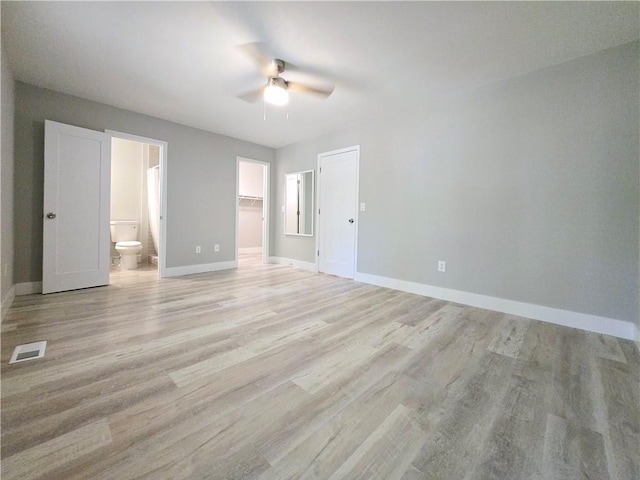 unfurnished bedroom with ensuite bath, a spacious closet, a closet, ceiling fan, and light hardwood / wood-style floors