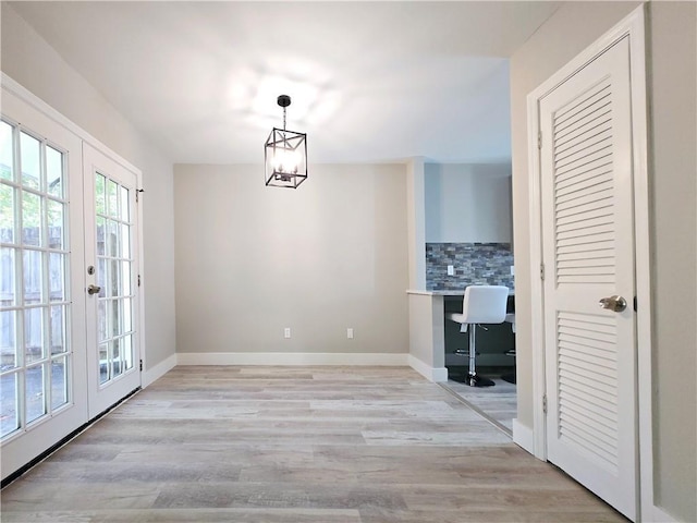 unfurnished dining area with an inviting chandelier, built in desk, light hardwood / wood-style flooring, and french doors