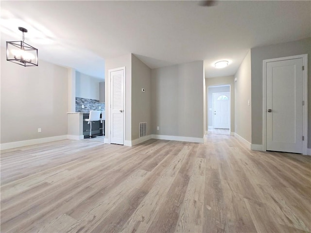 unfurnished living room featuring an inviting chandelier and light hardwood / wood-style flooring