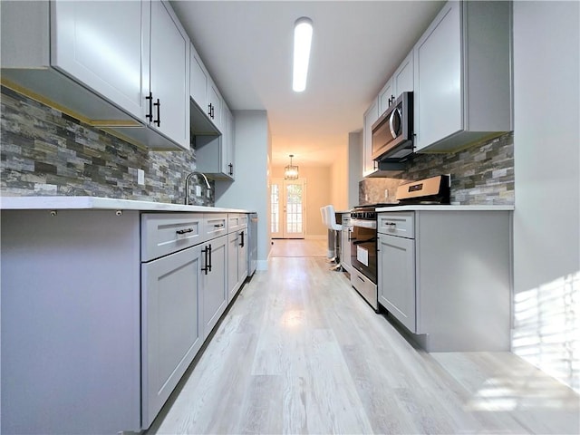 kitchen with light hardwood / wood-style flooring, decorative backsplash, gray cabinets, and stainless steel appliances