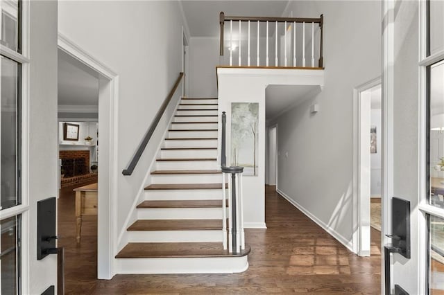 foyer featuring ornamental molding, stairs, wood finished floors, baseboards, and a high ceiling