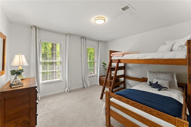 bedroom featuring baseboards, light carpet, a textured ceiling, and visible vents