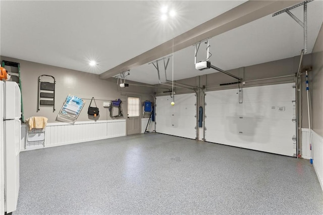 garage featuring freestanding refrigerator, a garage door opener, and a wainscoted wall