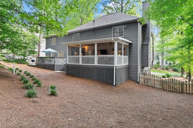 rear view of house featuring fence, a chimney, a sunroom, and a deck