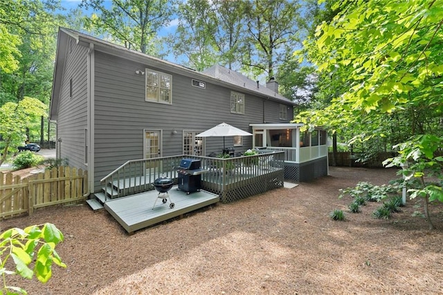 rear view of house featuring fence, a chimney, a sunroom, and a wooden deck