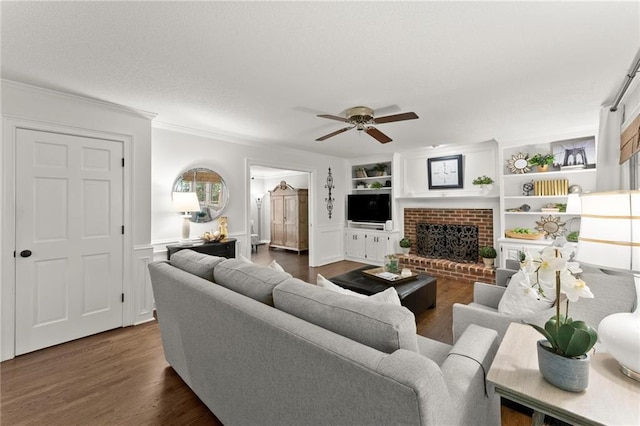 living room featuring ceiling fan, built in features, wainscoting, a brick fireplace, and dark wood-type flooring